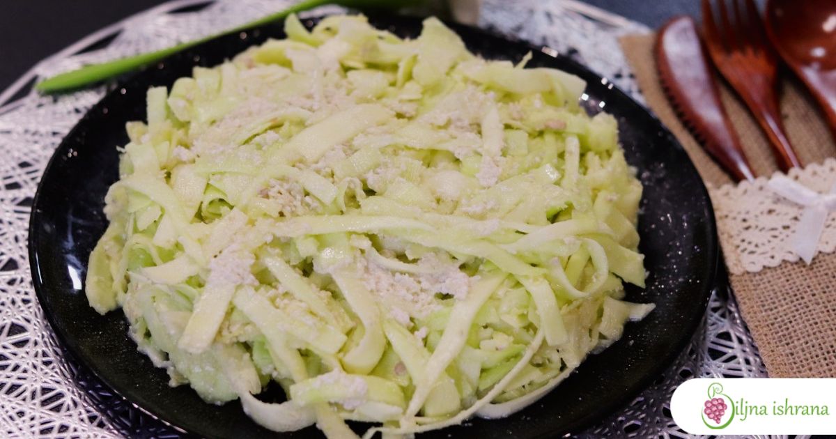 Fettuccine Alfredo u sirovom veganskom izdanju na crnom tanjiru. Pored tanjira je drveni escajg, a iznad tanjira je salveta u ukrasnom držaču.