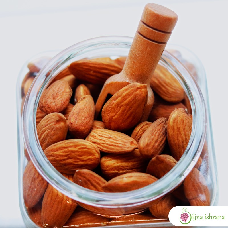 Bademi u staklenoj teglici sa drvenom lopaticom unutar teglice.