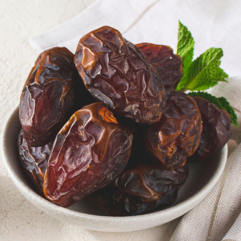 Medjool urme u beloj činijici, slikane od gore iz kosine. Sa gornje desne strane činije je par zelenih listića.