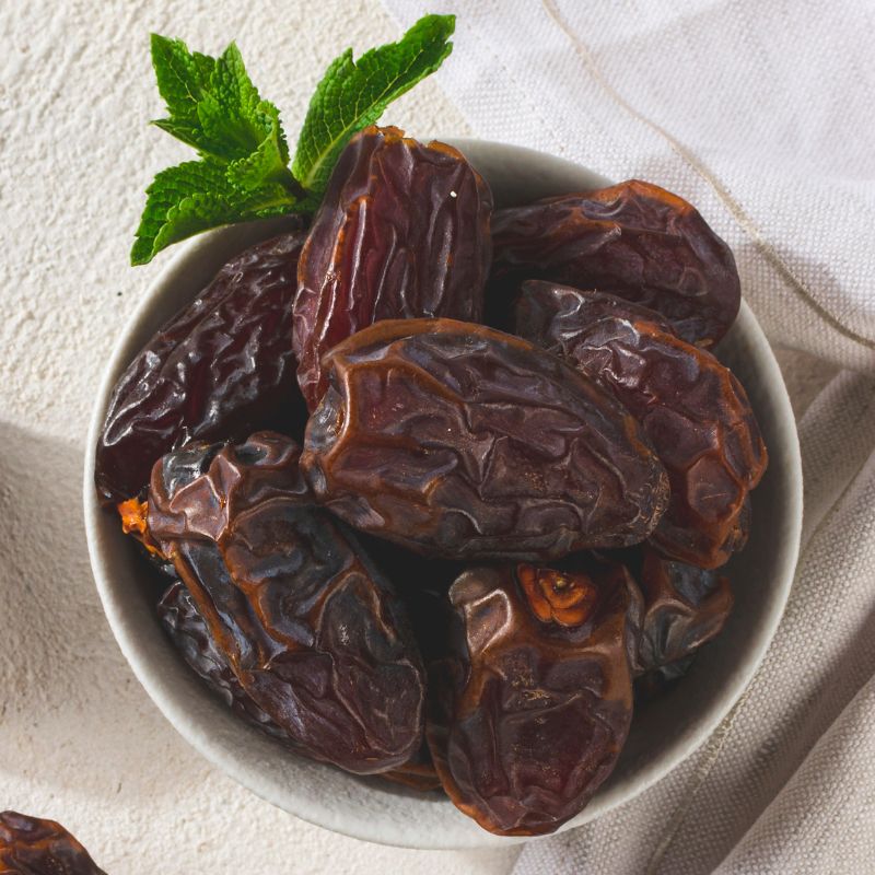 Medjool urme u beloj činijici, slikane od gore. Sa gornje leve strane činije je par zelenih listića.