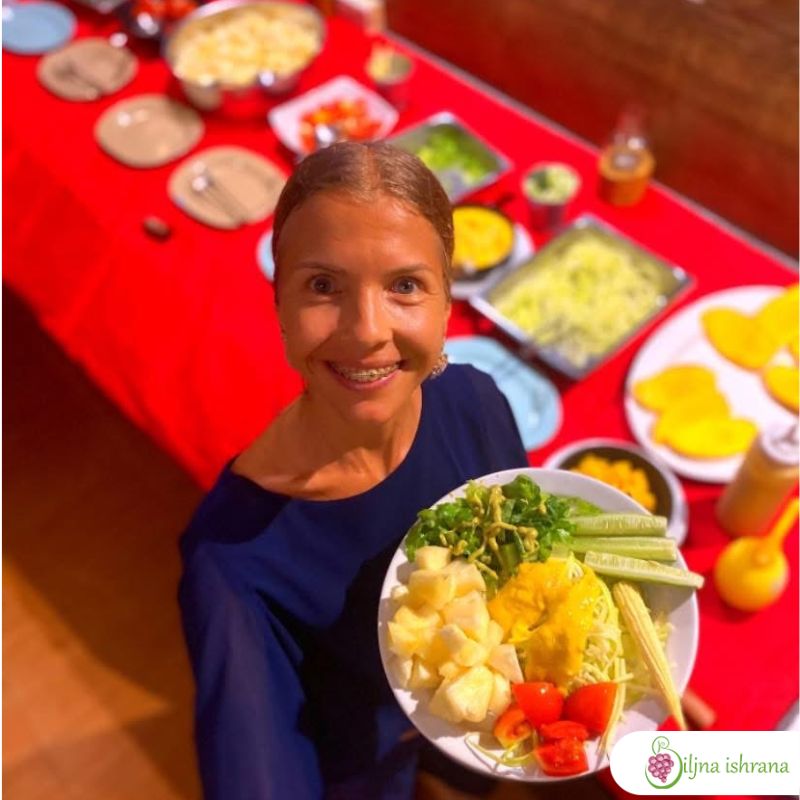 Marina sa Biljne ishrane drži tanjir pun sirove biljne ishrane i stoji pored švedskog stola na Tajlandskom ritritu Biljne ishrane.