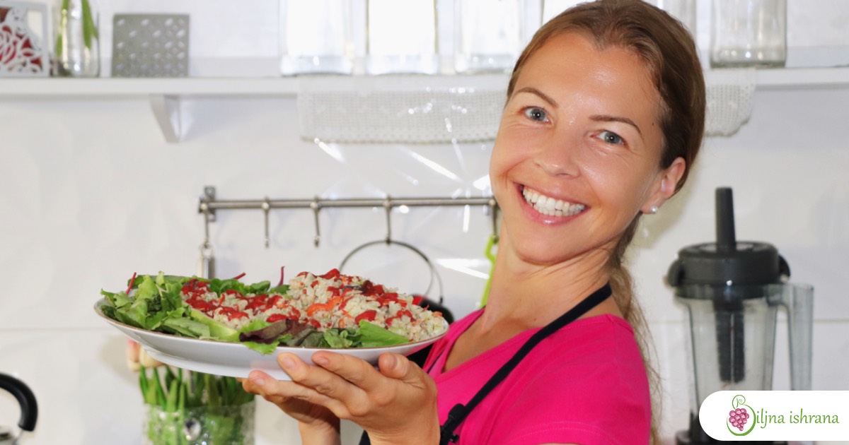 Marina sa 'Biljne ishrane', kreatorka onlajn programa 'Kulinarski čas - Sirova veganska večera' stoji u svojoj kuhinji bez šporeta, drži tanjir sa sirovom veganskom večerom i smeje se prema kameri.