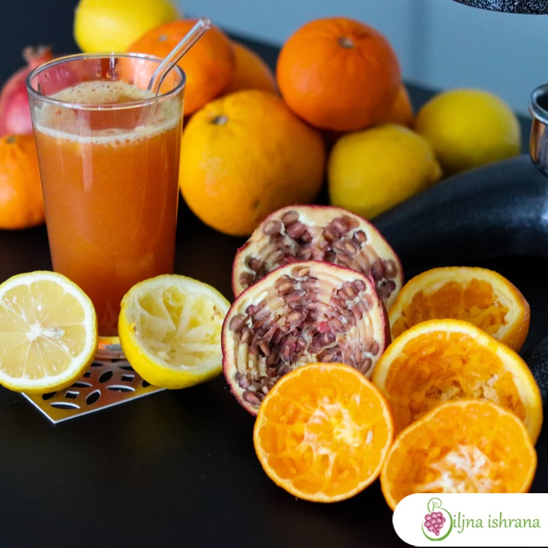 Čaša puna soka od nara, grejpa, narandže i limuna. U čaši je i staklena slamčica. Pored ćaše je citrusno voće i isceđene kore citrusnog voća.