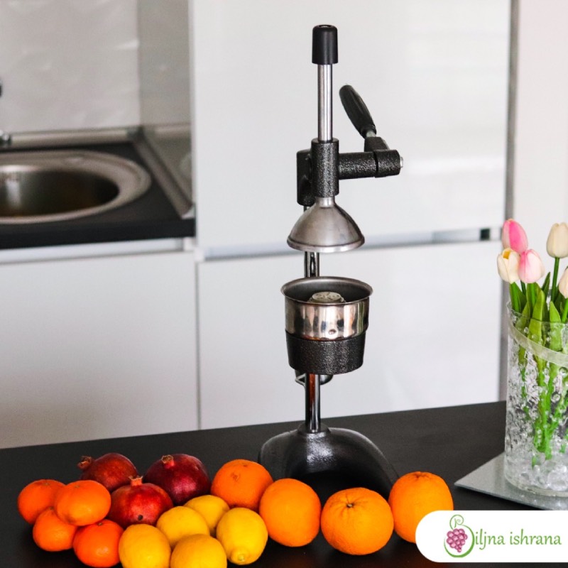 Presa za ceđenje nara stoji na kuhinjskom pultu. Pored prese je citrusno voće i isceđene kore nara, limuna, narandže i grejpa. Sa desne strane slike vidi se staklena vaza sa lalama.