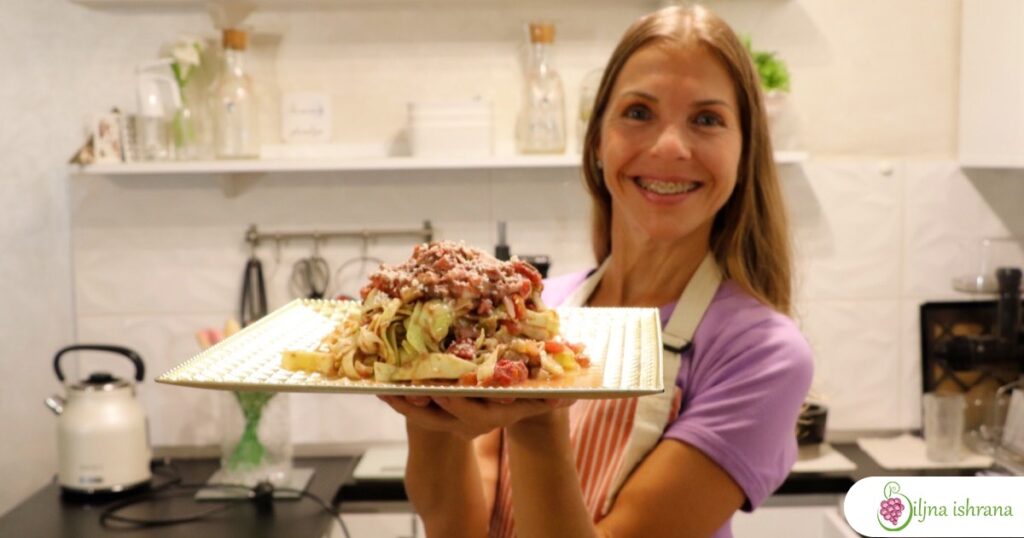 Marina sa Biljne ishrane drži tanjir na kojem je sirova veganska pasta taljatele u bologneze sosu.
