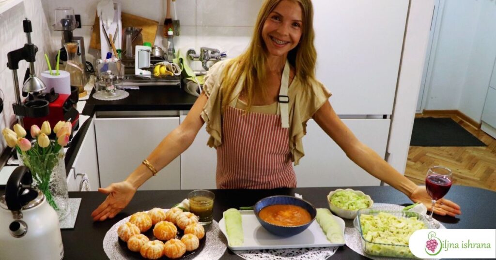 Marina sa Biljne ishrane stoji u svojoj kuhinji iza pulta na kojem su izložena tri sirova veganska obroka: doručak, ručak i večera.