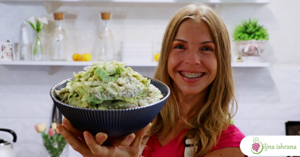 Marina sa Biljne ishrane drži činiju sa sirovim veganskim makaronima sa sirom.