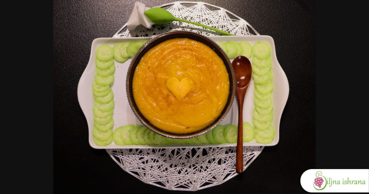 Primer ručka na sirovoj biljnoj ishrani slikan od gore. Puding od japanskih jabuka i krastavac, uz drvenu kašiku, salvetu u ukrasnom držaču, na beloj tacni, srebrnom podmetaču i crnom stolu.