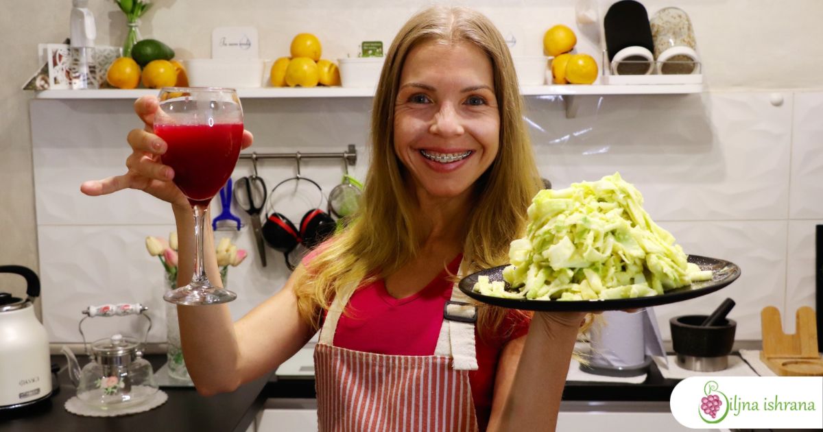 Marina sa Biljne ishrane drži vinsku čašu punu soka od nara u jednoj ruci i tanjir sa sirovom veganskom pastom u drugoj ruci.