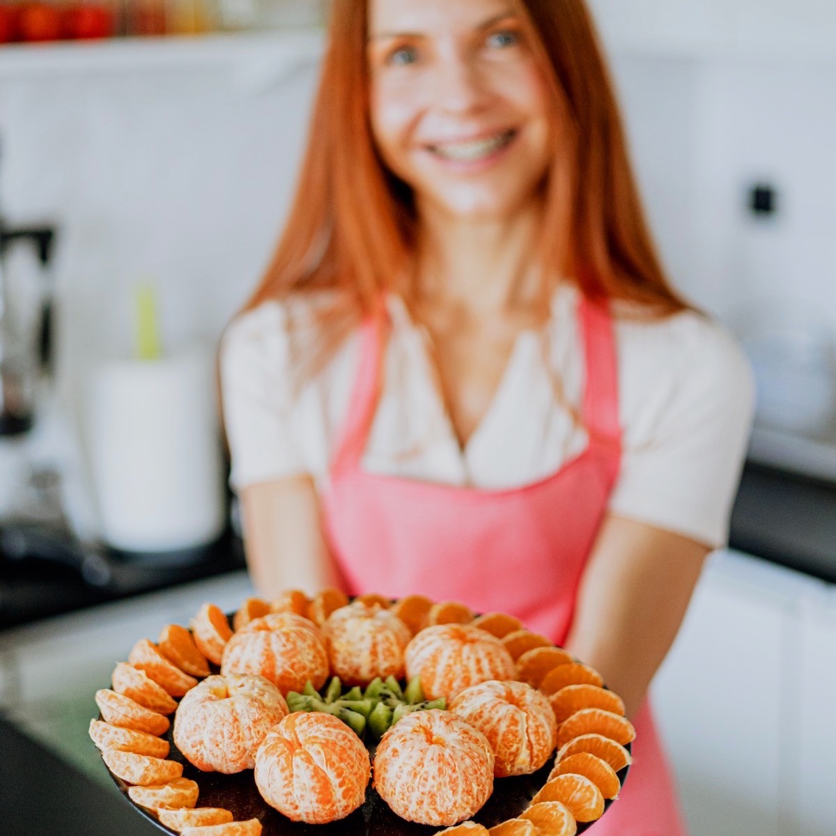 Marina sa Biljne ishrane stoji u svojoj kuhinji bez šporeta i drži tanjir pun mandarina i kivija.